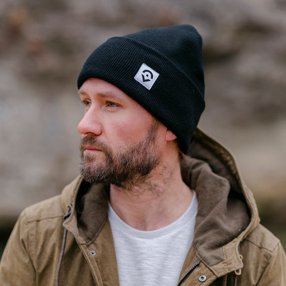 Outsider Black Ribbed Knit Beanie with White Logo modeled in the outdoors by a man