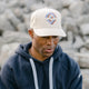 Cream colored hat with rainbow embroidered Outsider logos on the front modeled on a man