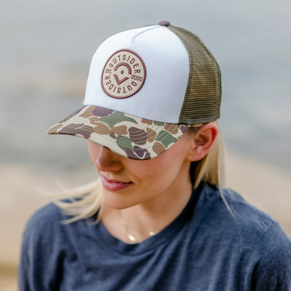 Outsider Adjustable Snapback Camo hat with camouflage bill and white front panel with Outsider patch modeled on woman